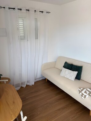 Una sala de estar moderna con un sofá color beige, una mesa redonda de madera y una cortina blanca.