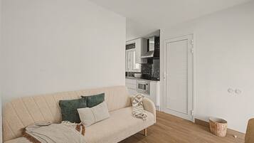A living room with a sofa, a kitchen in the background, and a wooden floor.