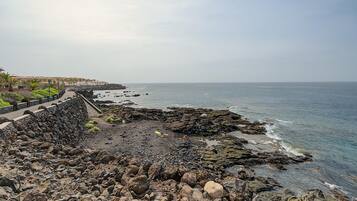 A rocky coastline with a paved walkway and buildings in the background.