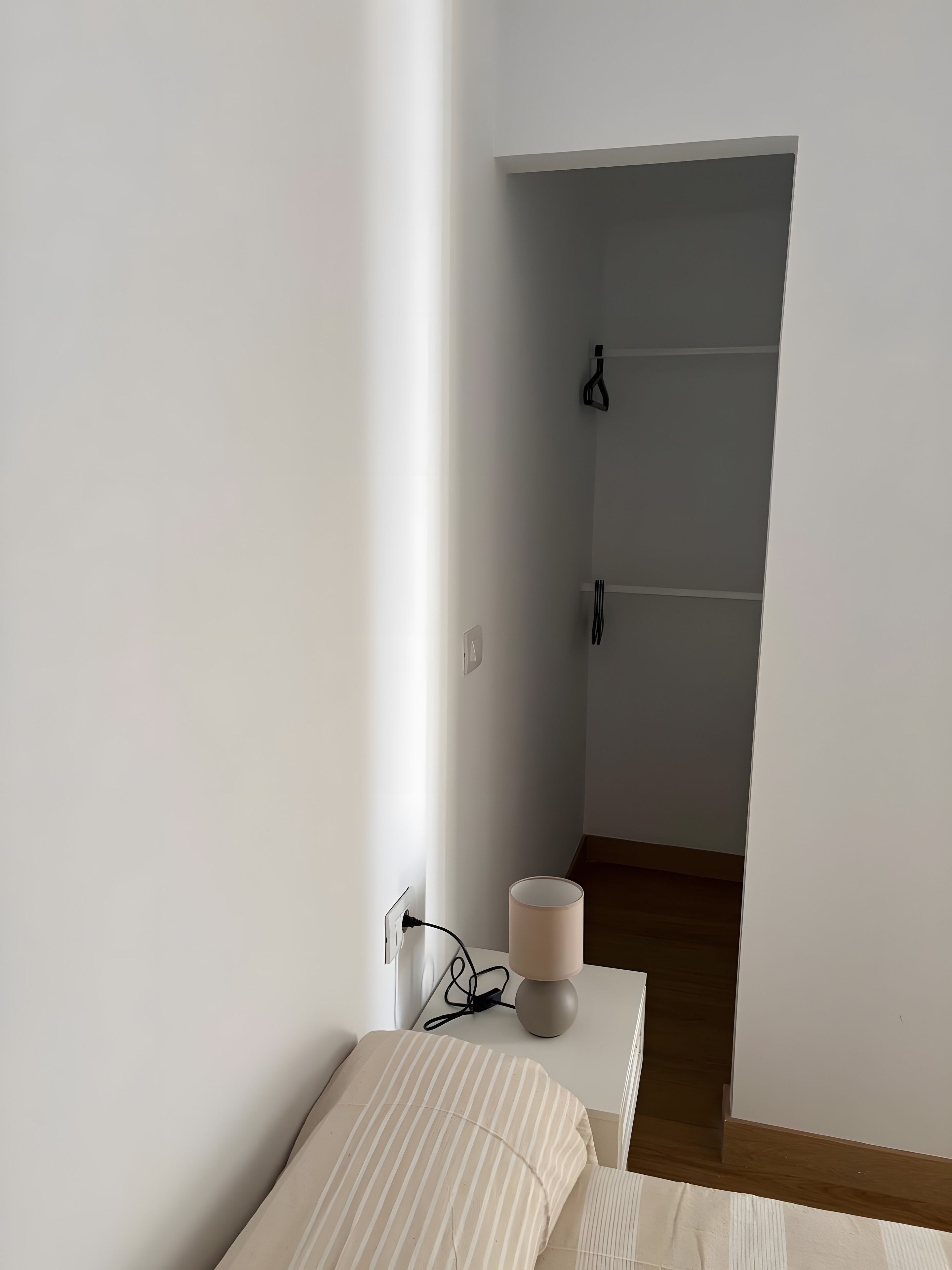 Een strak ingerichte kamer met een bed, een bedlampje en een stopcontact.