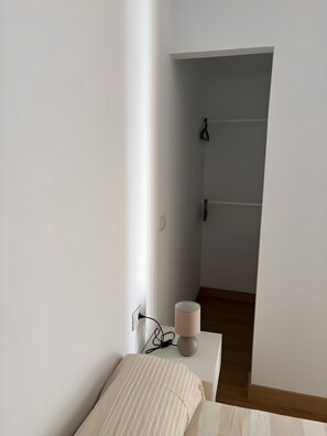 Una habitación minimalista con una cama, una lámpara de noche y un enchufe.