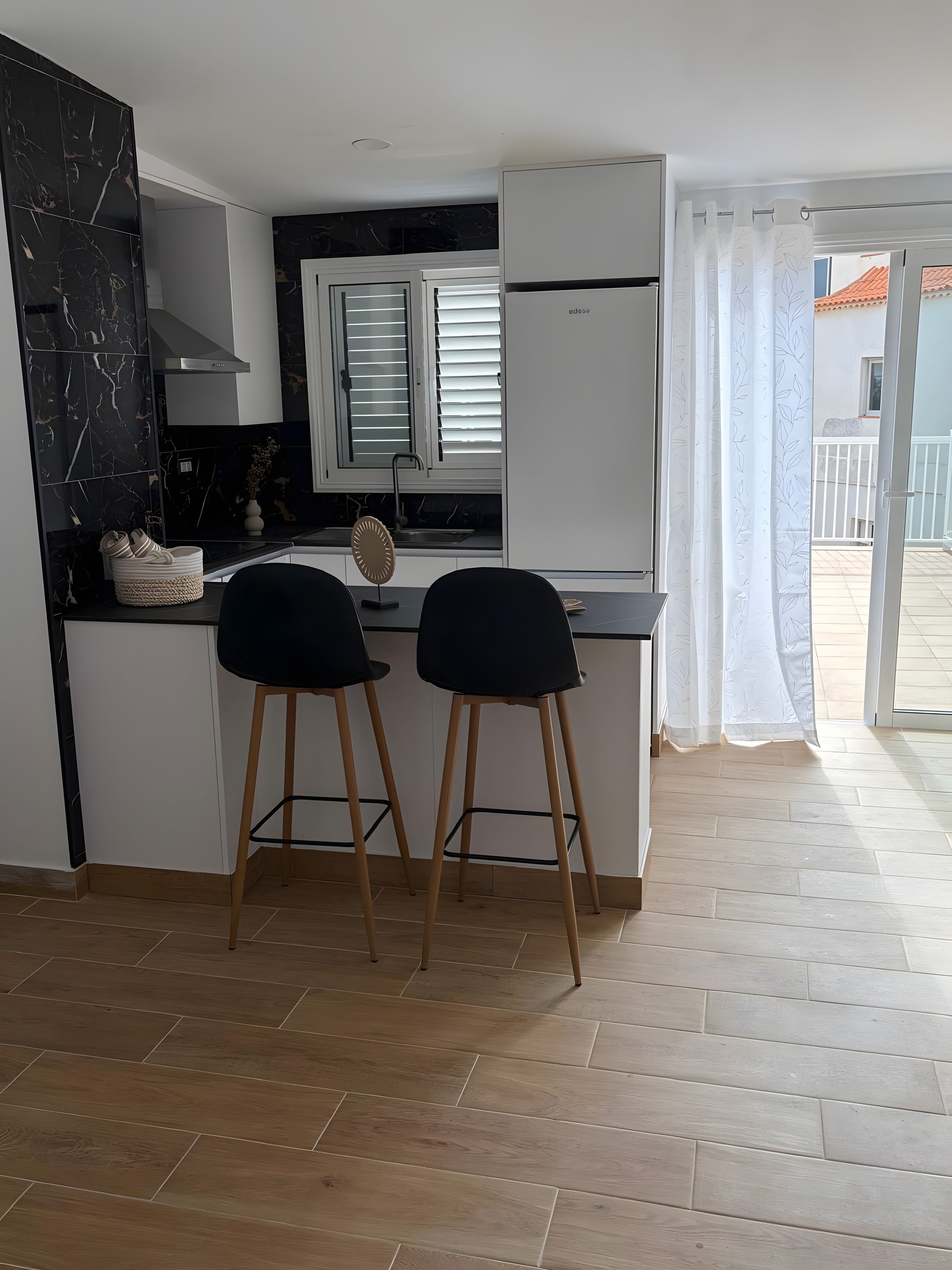 Una cucina moderna con due sgabelli neri, una schienale in marmo nero e una finestra con persiane.