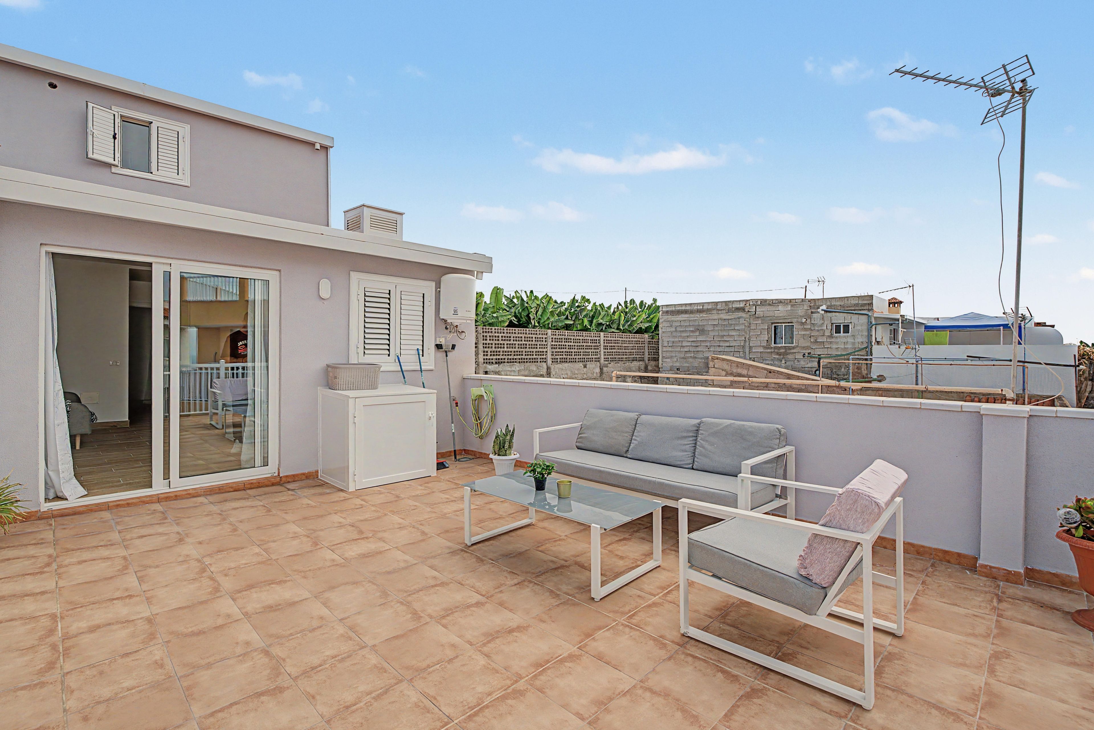 Un patio residencial con un sofá, una mesa y un  puerta corrediza de vidrio que da a una cocina.