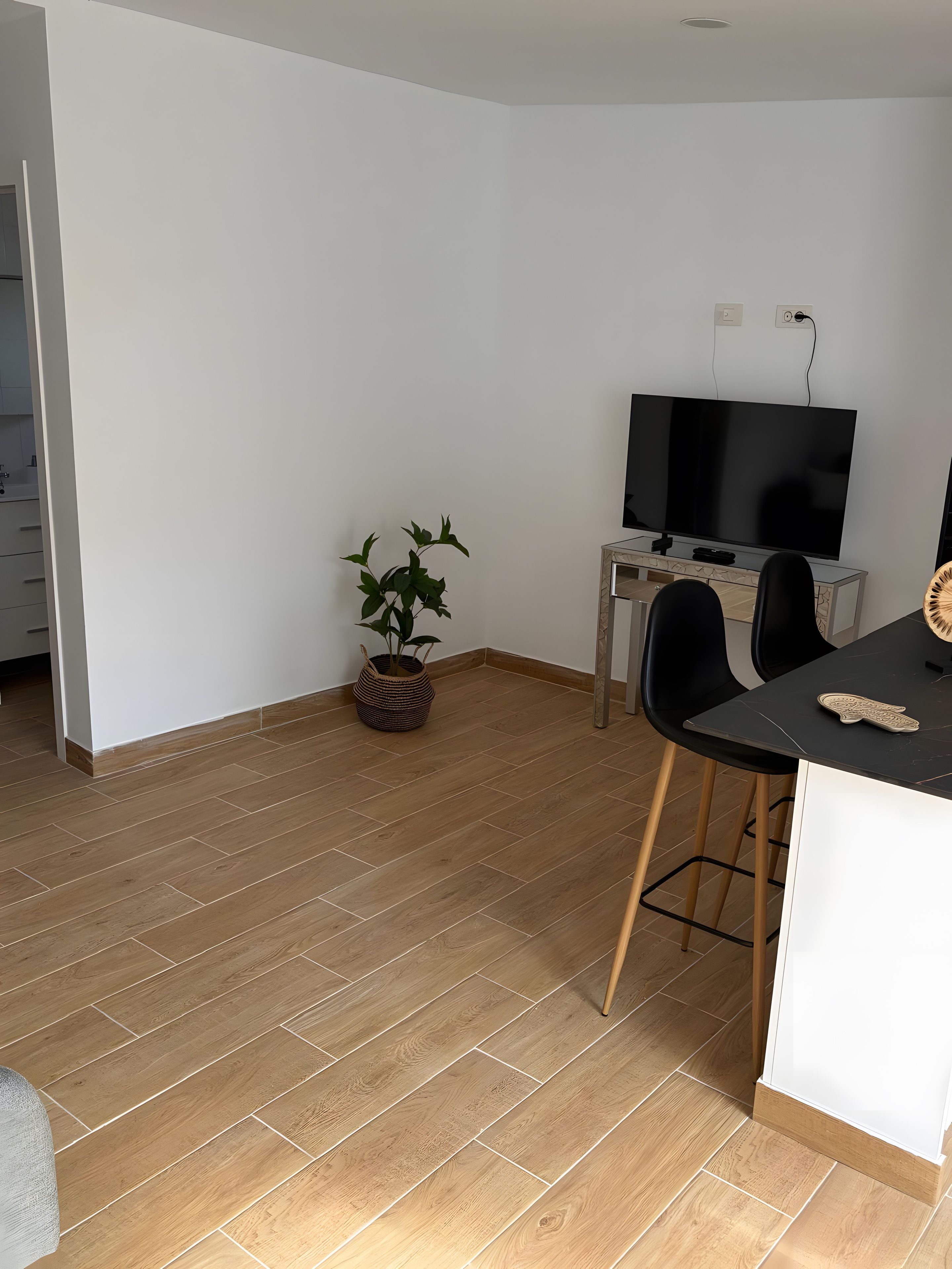A modern kitchen with a wooden floor, a dining area with a black table and chairs, and a TV on a stand.