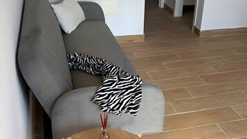 Ein modernes Wohnzimmer mit einem grauen Sofa, einer Zebra-Decke, einem kleinen Holztisch mit einer Topfpflanze und einem Holzboden.