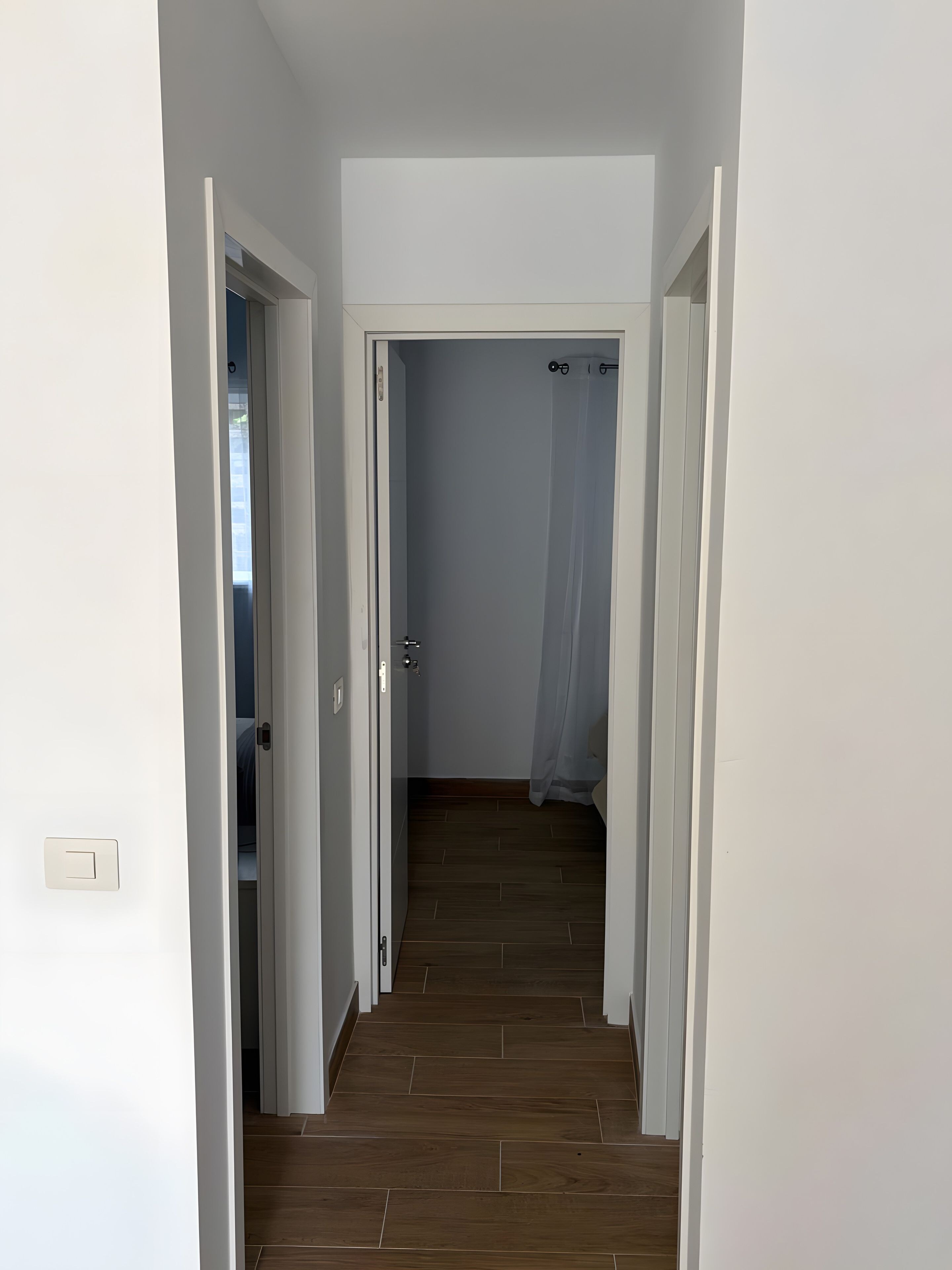 Un pasillo con piso de madera y paredes blancas que conduce a una habitación con cama y baño.