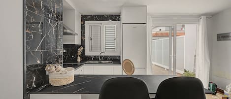 A modern kitchen with a black marble backsplash, white cabinets, and a built-in oven. There are two black chairs at the kitchen counter.