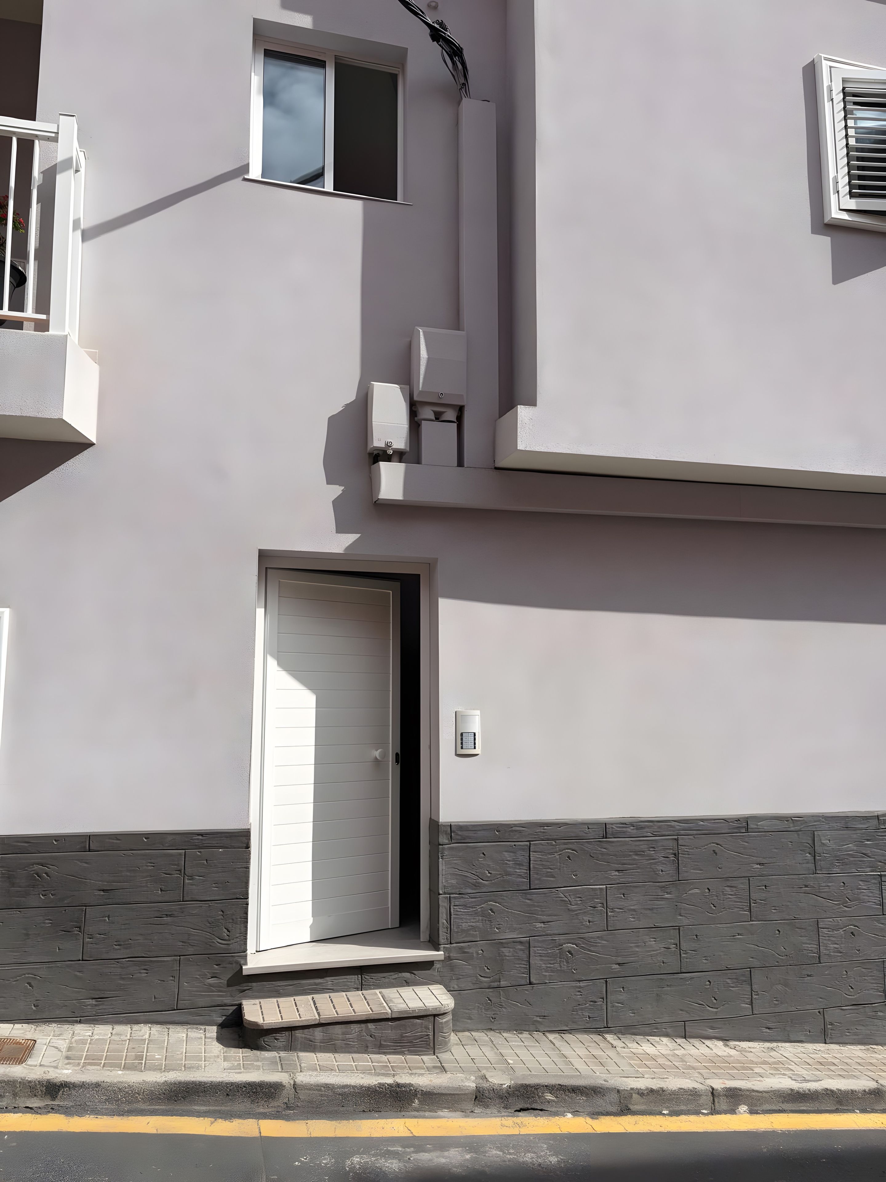 Fachada de edificio con puerta blanca, una ventana pequeña y una cámara de seguridad.