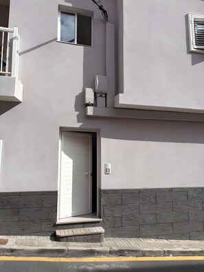 Une façade d’immeuble avec une porte blanche, une petite fenêtre et une caméra de surveillance.