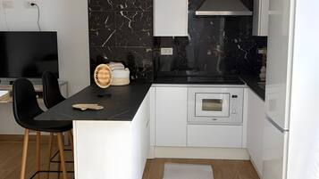 Una cocina moderna con salpicadero de mármol negro, muebles de color blanco y microondas integrado.