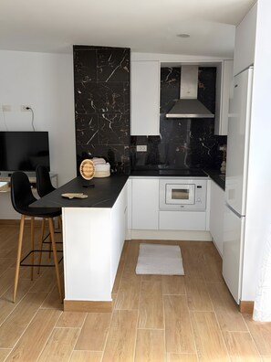 Une cuisine moderne avec un dosseret en marbre noir, des armoires blanches et un micro-ondes encastré.