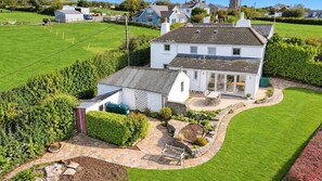 A white two-story house with a stone patio, a garden, and a fenced area with animals. - Penlows (Blackawton)