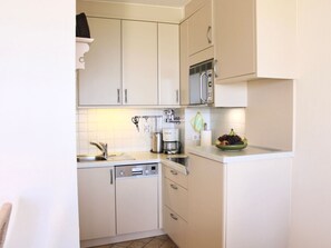 A compact kitchen with white cabinets, a microwave, a coffee maker, and a fruit bowl on the counter. - Apartment "tohus" (Wyk auf Foehr)