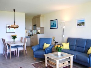 A compact living space with a dining area, a sofa set, a coffee table, and a kitchen in the background. - Apartment "tohus" (Wyk auf Foehr)