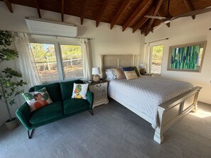 Ein Schlafzimmer mit einem Bett, einem grünen Sofa, einem Nachttisch und einem Fenster mit Vorhängen.