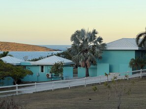 Ein Küsteneigentum mit einem türkisblauen Gebäude, einem weißen Zaun und Blick aufs Meer.