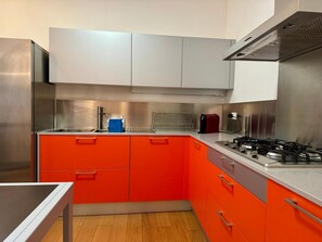 Una cocina con electrodomésticos de acero inoxidable, estufa a gas y gabinetes color naranja.