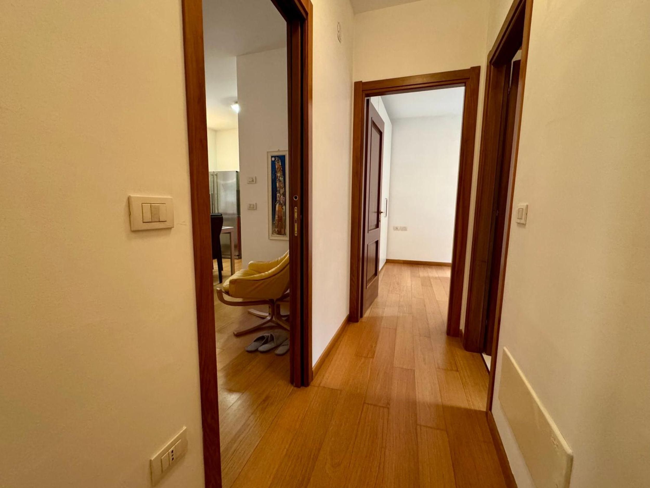 A hallway with wooden flooring, a chair, and a door leading to another room.