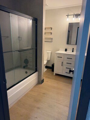 A bathroom with a glass-enclosed shower, a toilet, a sink with a mirror, and wooden flooring. - Villa Belle, a stylish retreat just 10 minutes from the Strip and the airport (Las Vegas)