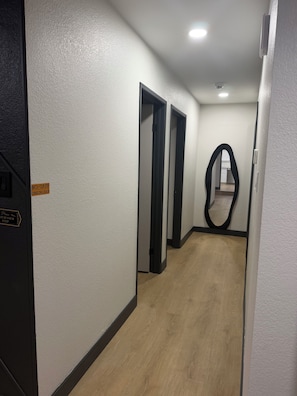 Un couloir aux murs blancs, doté d’un plancher en bois et de portes donnant sur d’autres pièces.