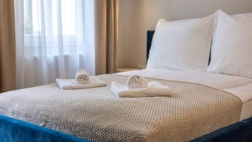 Una cama bien hecha con sábanas blancas y una colcha azul, una toalla enrollada y un almohadón sobre la cama.