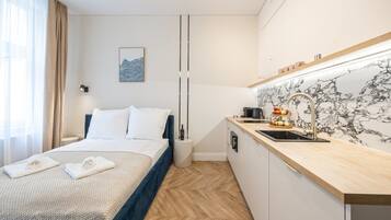A hotel room with a bed, a bedside table, a small kitchen area with a sink, and a marble backsplash.