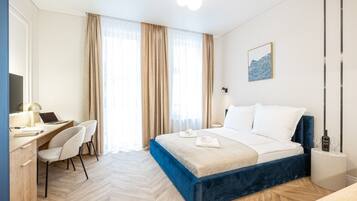A hotel room with a bed, desk, chair, and a painting on the wall.