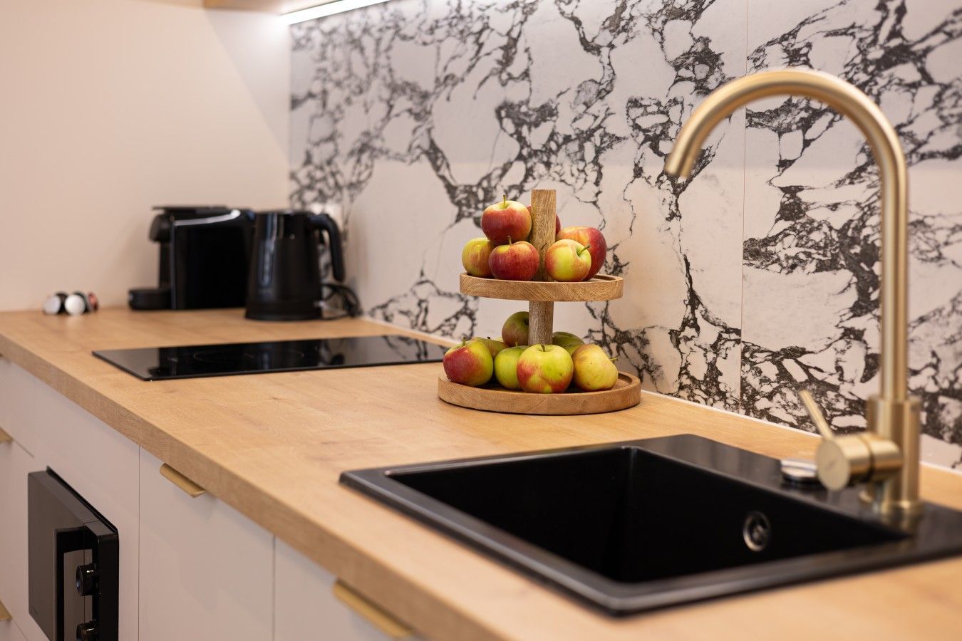 Una cocina con salpicadero de mármol, un frutero de madera, un lavabo negro y una cafetera.