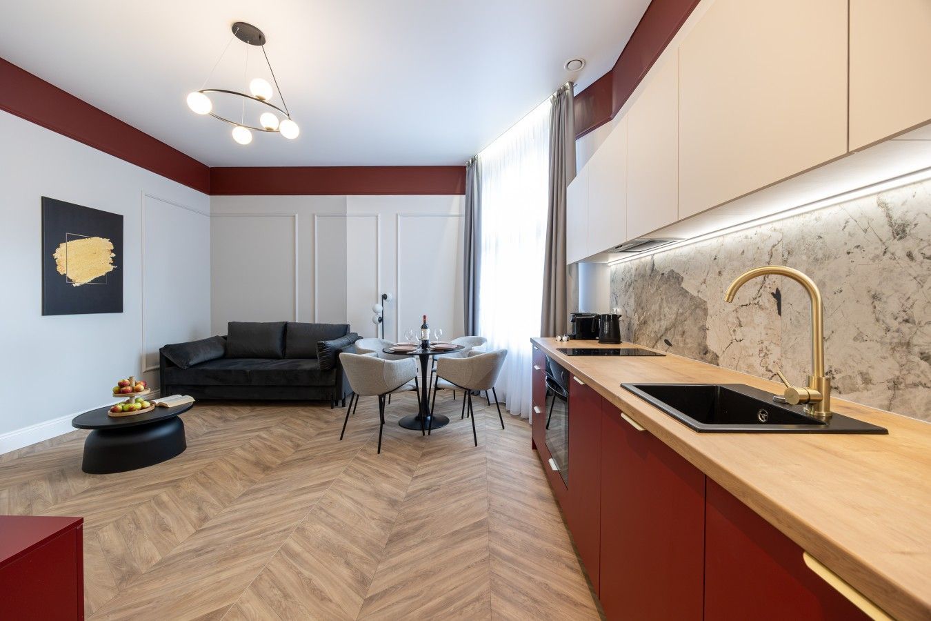 A modern kitchen with a herringbone floor pattern, a dining area with a round table and chairs, and a dark-colored sofa.