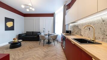 A modern kitchen with a herringbone floor pattern, a dining area with a round table and chairs, and a dark-colored sofa.