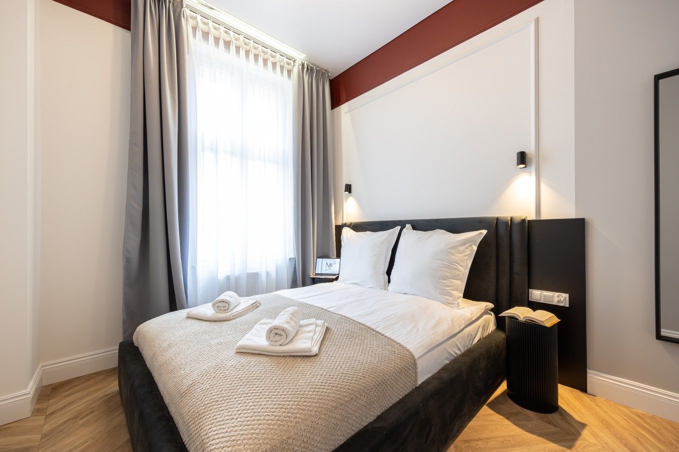 A hotel room with a large bed, a bedside table, a nightstand, a lamp, and a window with curtains.