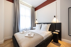 Quarto de hotel com uma cama grande, mesa de cabeceira, abajur e janela com cortinas.
