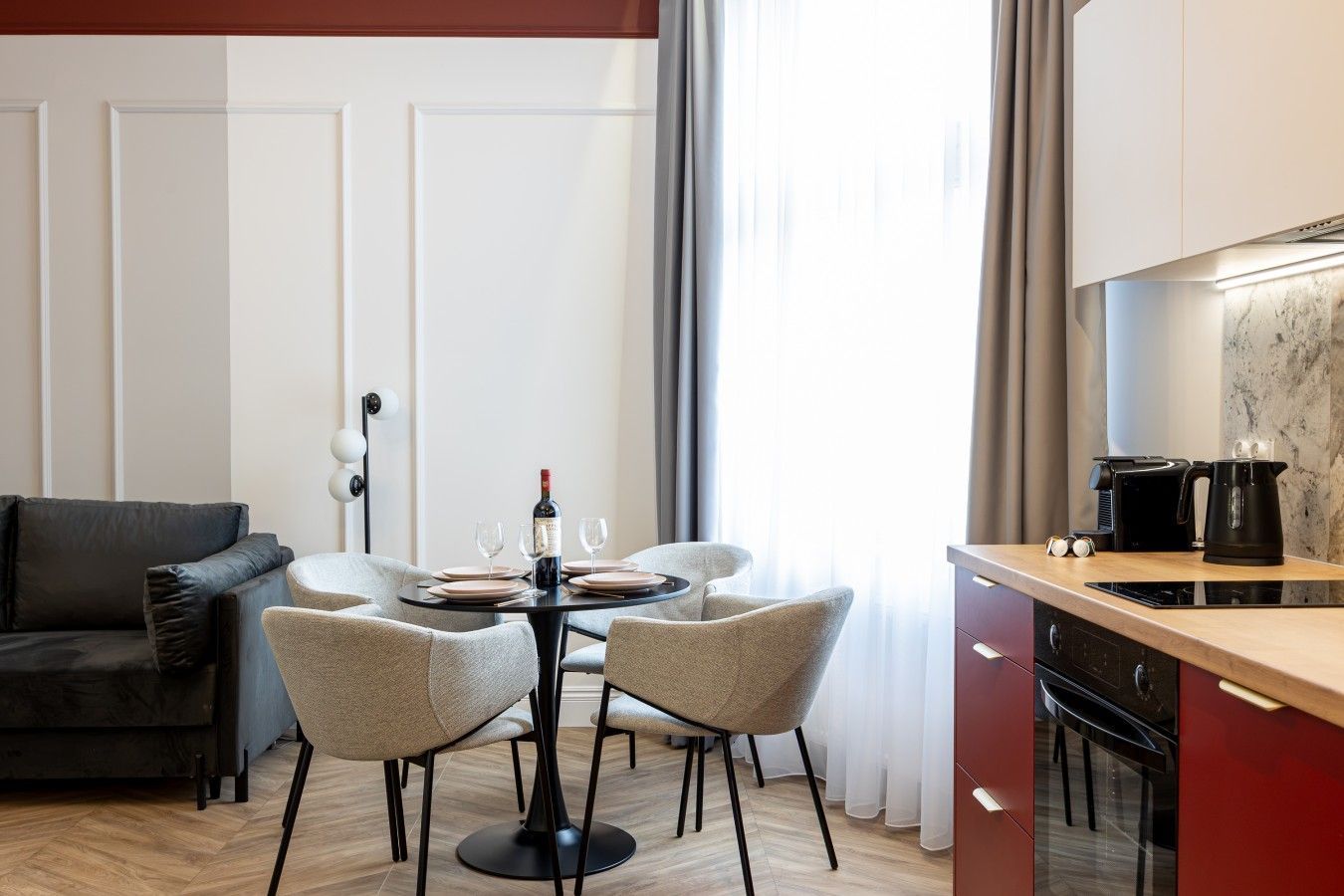 Una sala moderna con un sofá de cuero oscuro, una mesa de comedor redonda con cuatro sillas y una zona de cocina con estufa y cafetera.