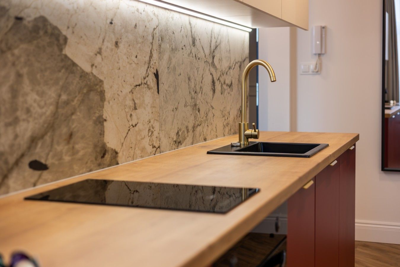 A kitchen with a marble backsplash, a wooden countertop, a gold faucet, and a black sink.
