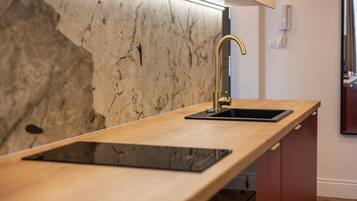 A kitchen with a marble backsplash, a wooden countertop, a gold faucet, and a black sink.