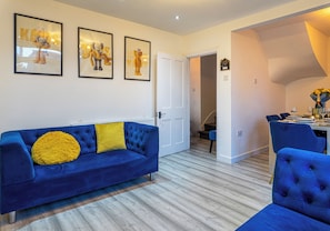 Una sala de estar moderna con un sofá azul, un cojín amarillo y obras de arte enmarcadas en la pared.