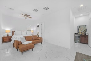Ein modernes Wohnzimmer mit einem braunen Ledersofa, einem Deckenventilator und einem Essbereich mit einer Glaskabine.