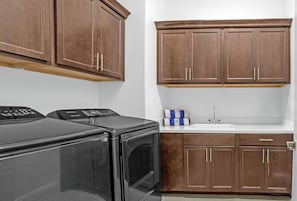 A laundry area with a washing machine and dryer, a sink with a faucet, and wooden cabinets above and below the sink. - Lake Las Vegas Home (Henderson)