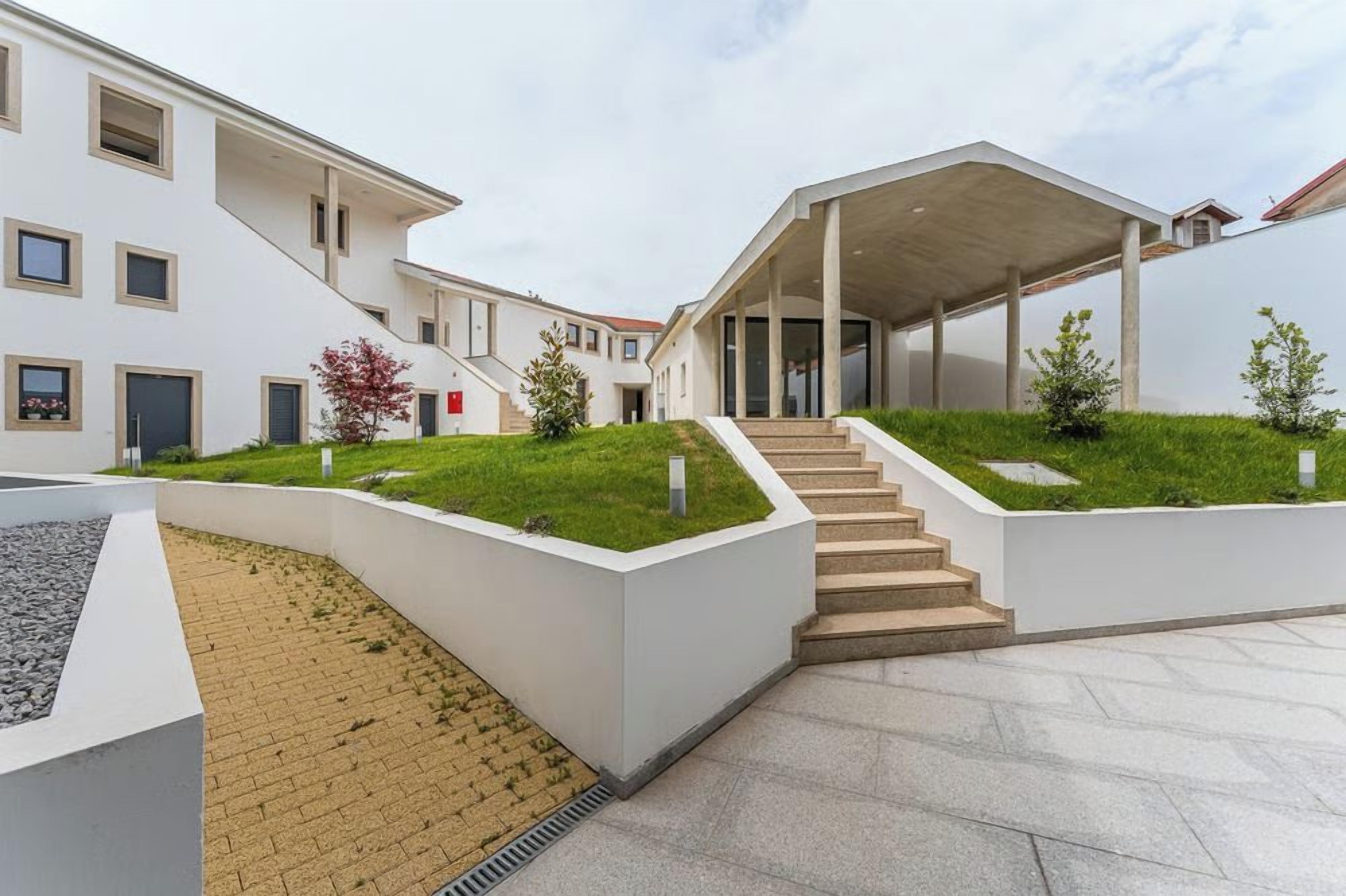 A modern building with a covered staircase, a flat roof, and a landscaped area with grass and shrubs.