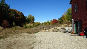 A gravel driveway leading to a red building with a covered outdoor seating area and a solar-powered device. - Quiet Property w/ Private Entrance (Weare)