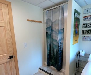 A hallway with a wooden door, a shower curtain with a mountain design, and a wall with various signs and a toilet paper holder. - Quiet Property w/ Private Entrance (Weare)