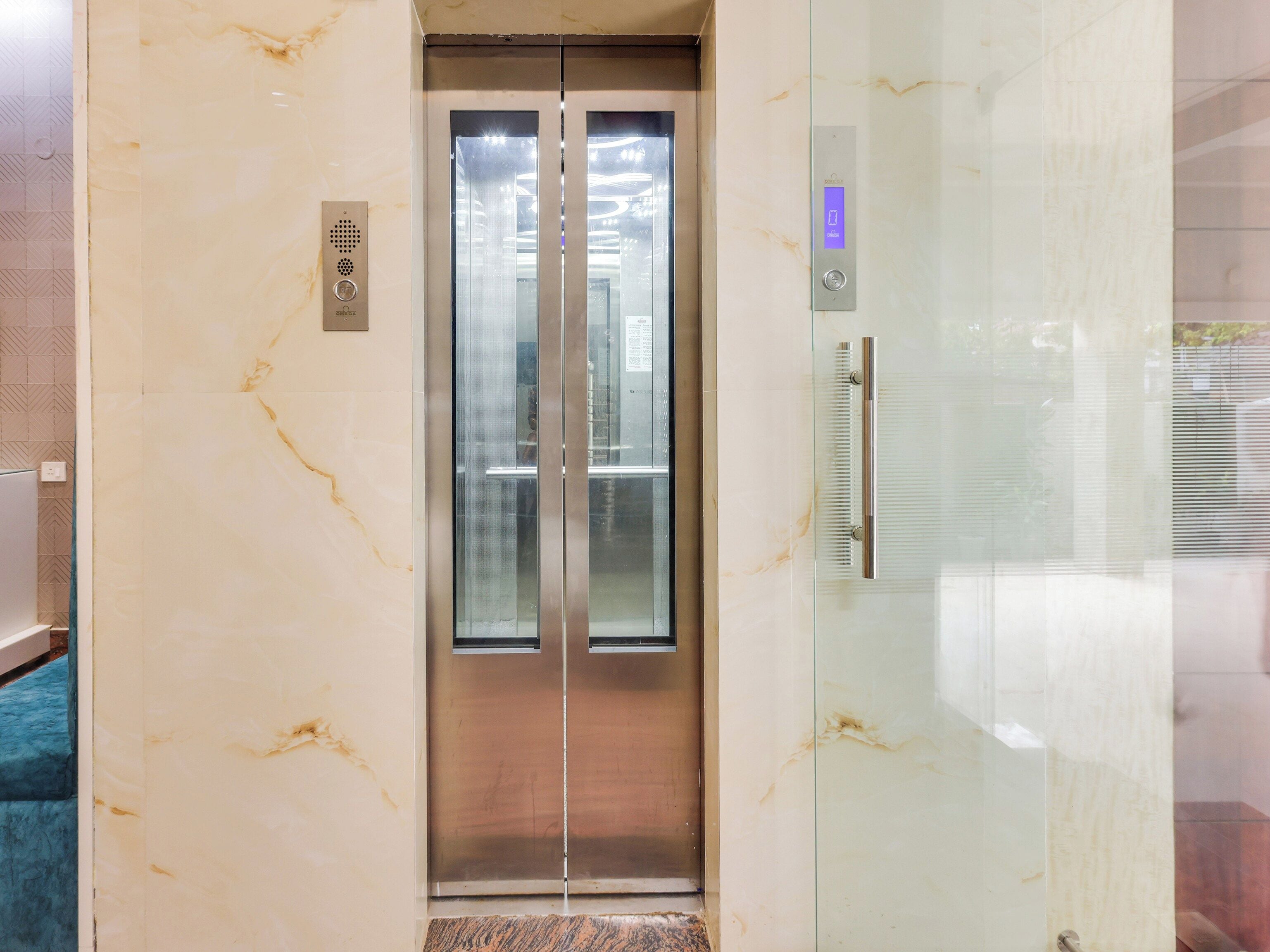 An elevator with a metallic finish, a control panel with a button, and a glass door with a handle.