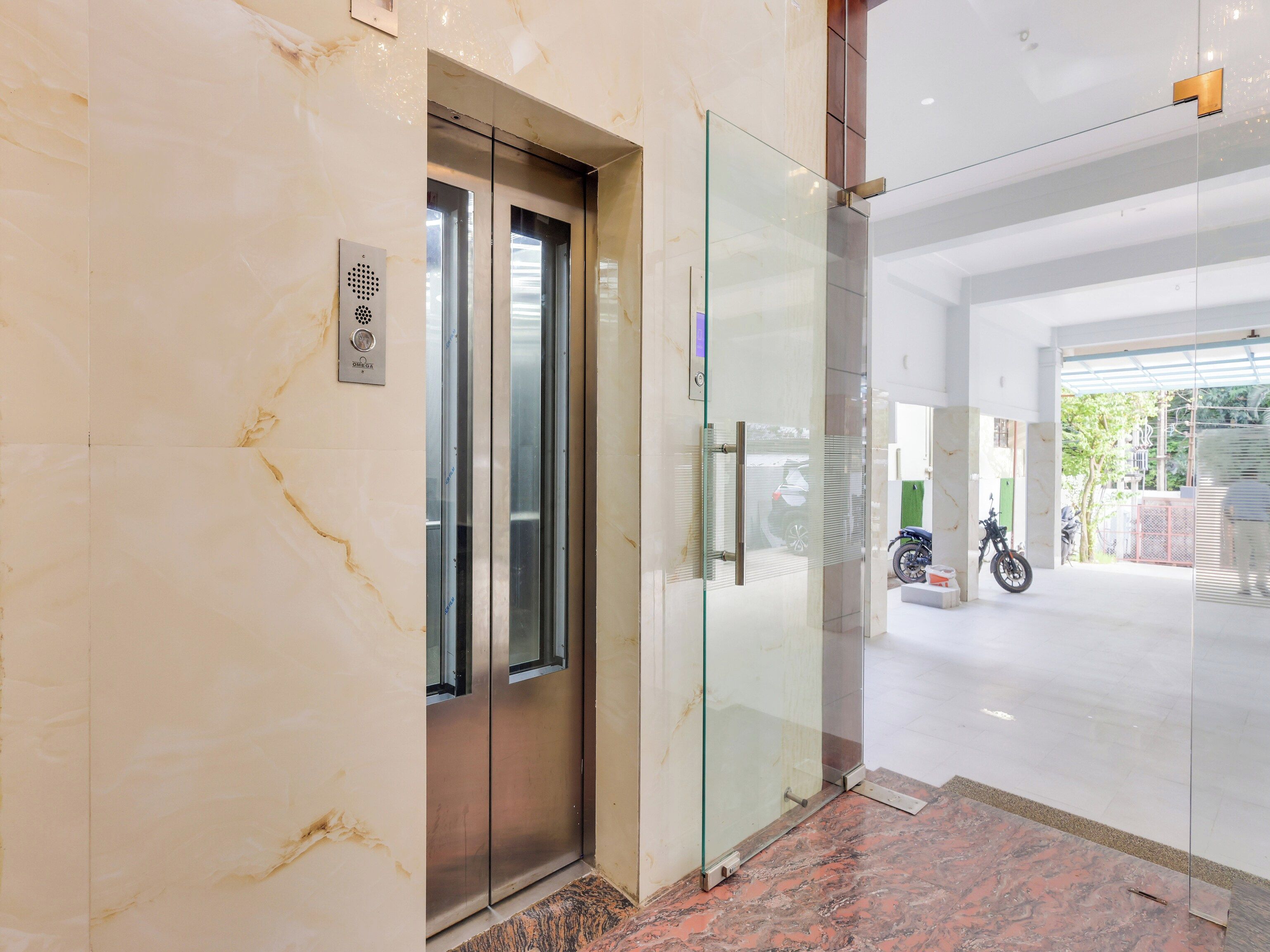 A modern elevator with a glass door, a marble floor, and a visible motor room.