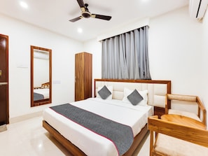A hotel room with a bed, a wooden wardrobe, a mirror, a ceiling fan, and a window with curtains. - Townhouse Royal Inn (Guwahati)