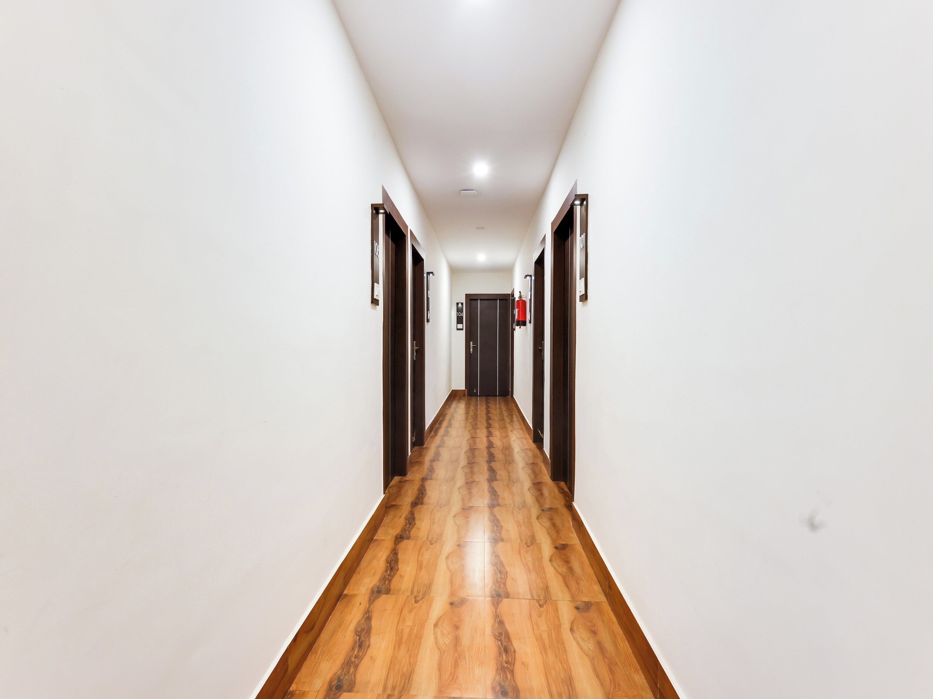 A long, narrow hallway with wooden flooring and white walls.