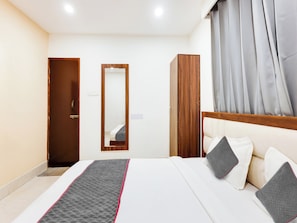 A hotel room with a bed, a wardrobe, a mirror, and a window with curtains. - Townhouse Royal Inn (Guwahati)