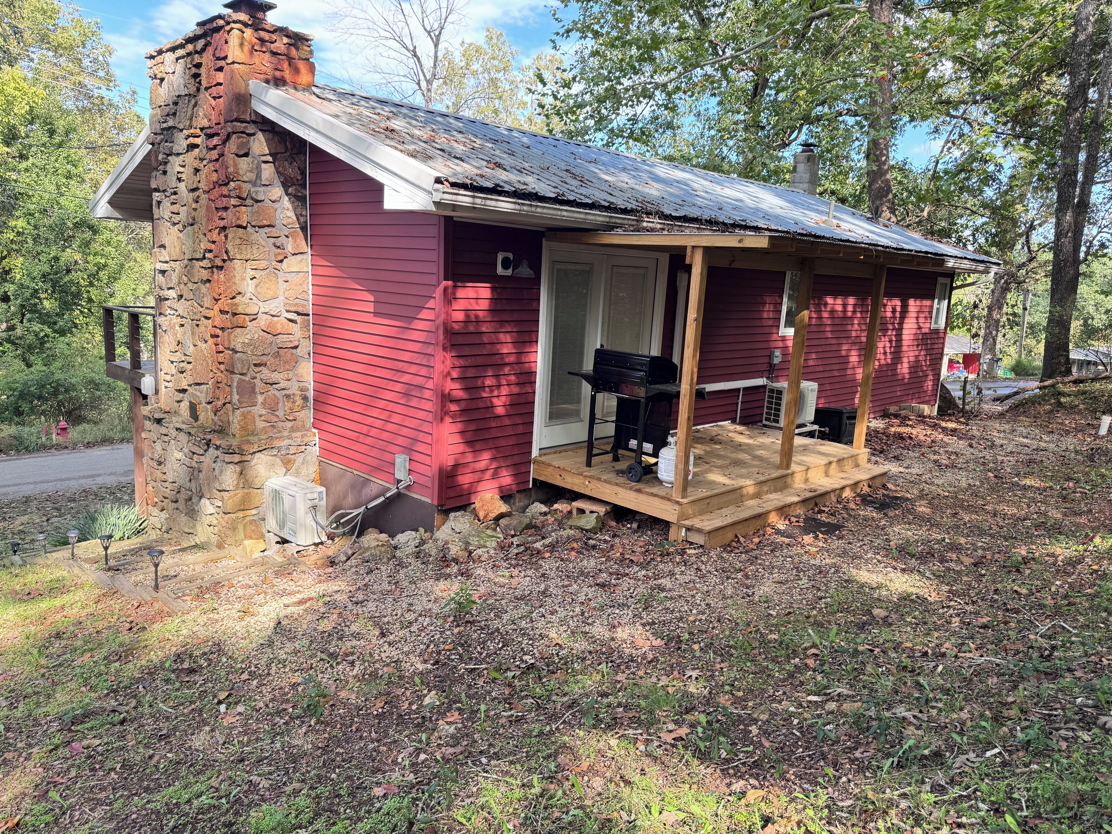 Une petite cabane avec une cheminée en pierre, une véranda et un barbecue à l’extérieur.