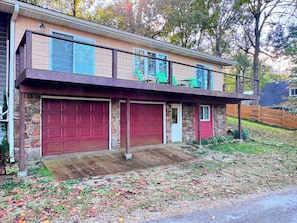 A two-story house with a stone facade, a red garage door, and a balcony with green chairs. - Cozy 2-bedroom cabin in beautiful Mammoth Spring (Mammoth Spring)