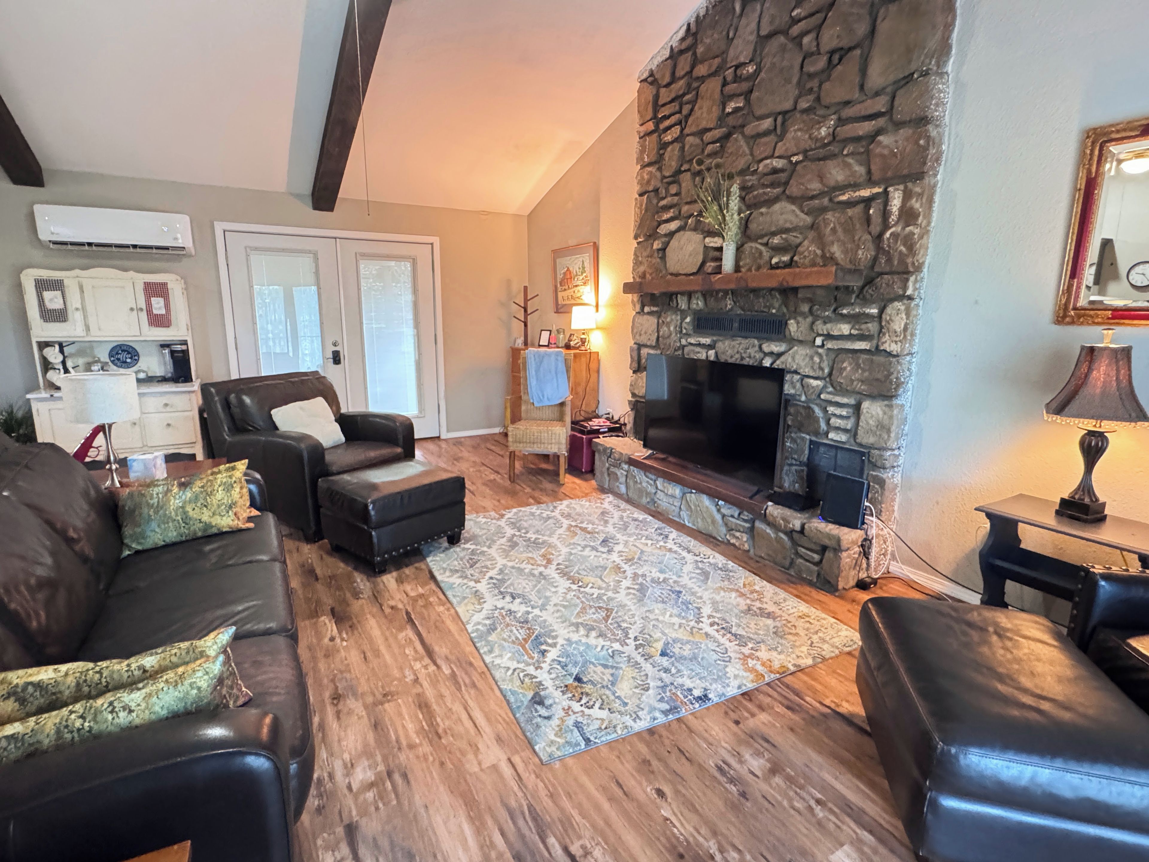 A living room with a stone fireplace, leather sofas, a patterned rug, and a television.