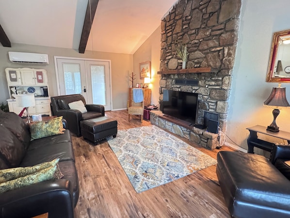 A living room with a stone fireplace, leather sofas, a patterned rug, and a television.